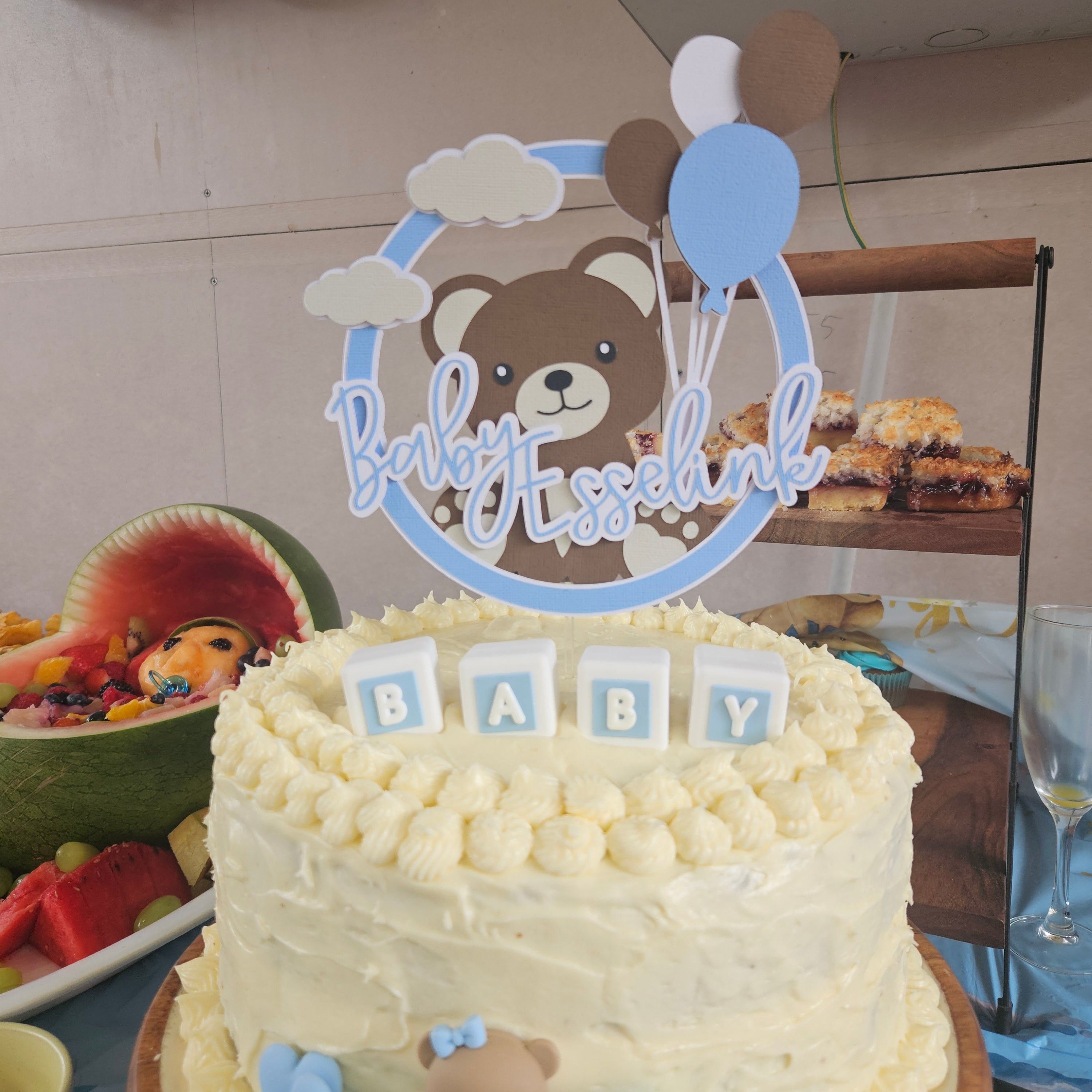 Baby shower cake with teddy bear topper and 'Baby' blocks on a table.